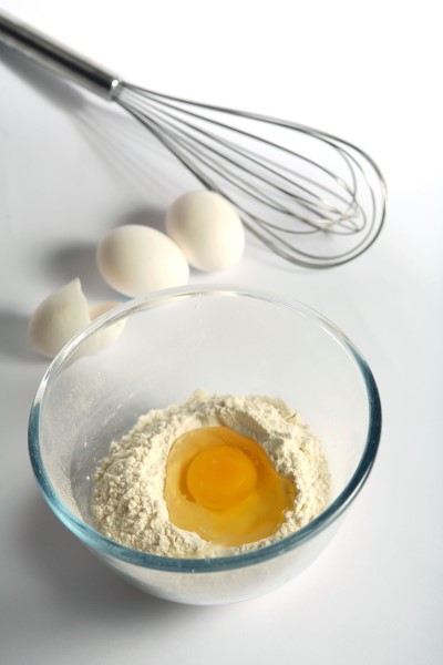 Un huevo roto en harina en un bol mezclar con otros huevos y detrás de una bata